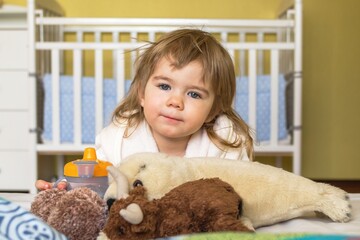 Adorable toddler girl in white robe playing with stuffed animals on bed