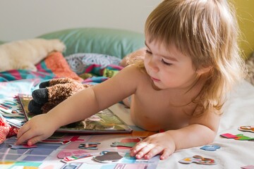 Adorable toddler girl playing with colorful puzzle pieces on a bed.