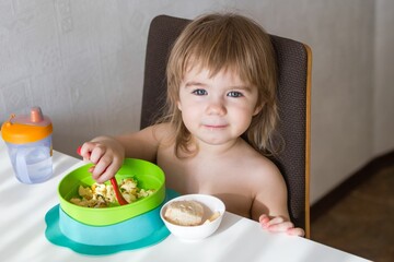 Sweet Toddler Girl Enjoying Scrambled Eggs and Toast for Breakfast in High Chair at Home - 792623709