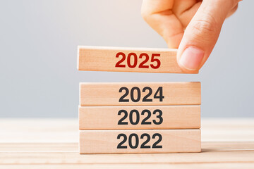 2025 block over 2024 and 2023 wooden building on table background. Business planning, Risk...