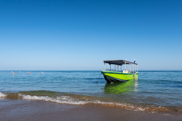 Small wooden green boat anchored on the beach with waves crushing against the shore, Fujairah,...