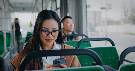 Camera view of beautiful Chinese girl sitting inside bus or train. Moving vehicle passing stop....