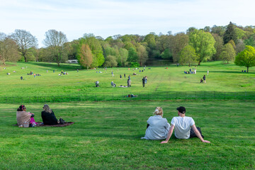 London. UK- 04.14.2023. Crowd of people relaxing and enjoying a day out on the green grass field of a park on a beautiful warm sunny Spring day.