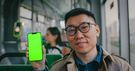 Handsome Chinese man sitting in middle of bus or train. Wearing glasses. Looking directly at camera...