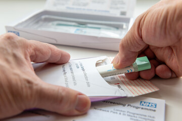 London. UK- 04.17.2024. A person putting the collected bowel cancer sample in the envelope to be sent off for testing. © Ming