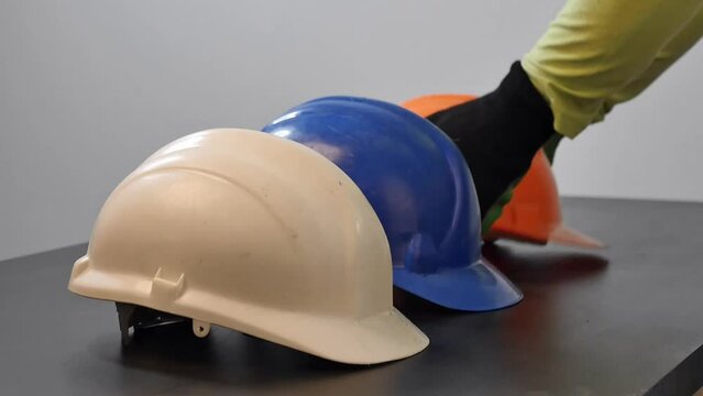 Closeup of four hard hats in white, blue, orange and yellow color, placed on a wooden surface in a row being picked up one-by-one by construction workers