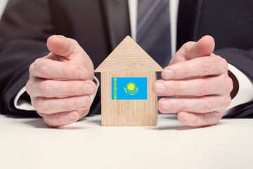 Businessman hand holding wooden home model with Kazakhstan flag. insurance and property concepts