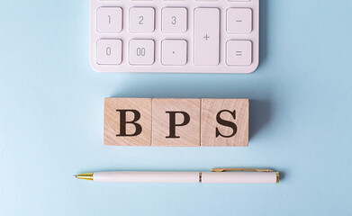 BPS word on wooden block with pen and calculator on blue background