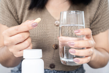 closeup woman hand taking vitamin c with a glass of water