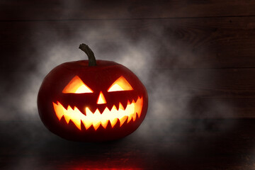 Spooky Halloween pumpkin, Jack O Lantern, with an evil face and eyes on a wooden table with a misty gray background.