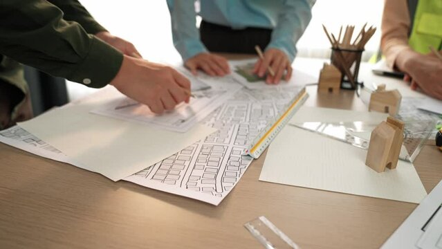 Smart architect and safety engineer discussion about building blueprint on table with architectural document, measurement tools and wooden block scatter around at modern office. Closeup. Delineation.
