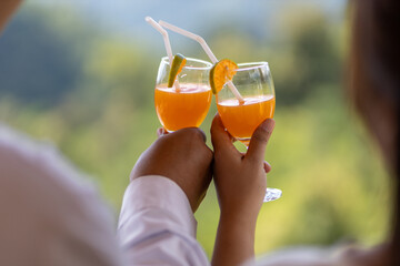 selective focus glasses of freshly squeezed orange juice in the hands of men and women clinking glasses of fresh tangerine juice Orange slices inserted into a glass