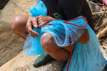 selective focus blue net in the hands of villagers catching fish along the river rapids in Thailand - obrazy, fototapety, plakaty