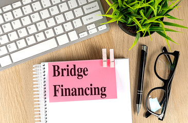 BRIDGE FINANCING text pink sticky on notebook with keyboard, pen and glasses