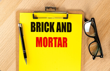 BRICK AND MORTAR text on yellow paper on clipboard with pen and glasses