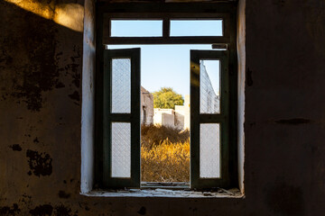 Damaged broken window overlooking courtyard in Al Jazirah Al Hamra abandoned town in Ras Al Khaimah, United Arab Emirates.