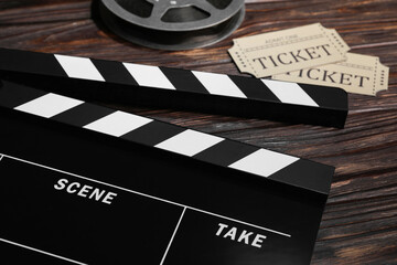 Clapperboard, movie tickets and film reel on wooden table, closeup