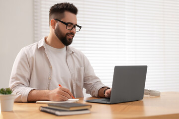 Young man in glasses watching webinar at table in room