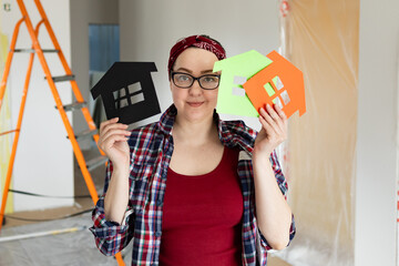 A friendly woman in glasses holds colorful paper houses in the air as a symbol of choosing new living quarters. High quality photo