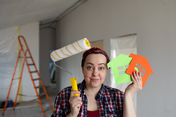 A woman with a roller in her hands and a paper house symbol is confused about choosing a painting color. High quality photo