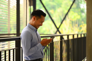 Smiling businessman using smartphone standing at the walkway inside a building