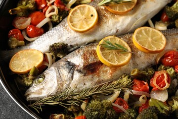 Baked fish with vegetables, rosemary and lemon on black textured table, top view
