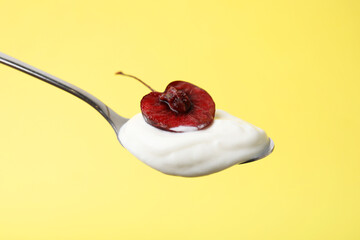Spoon with yogurt and cherry on yellow background, closeup