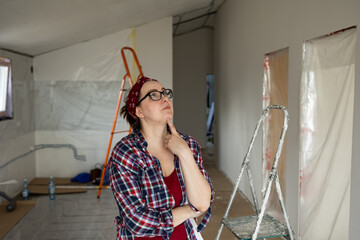 A woman in glasses and a plaid shirt thoughtfully examines the ceiling while appraising the painting job. High quality photo