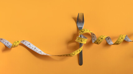 Fork with measuring tape on yellow background. Weight loss and healthy concept