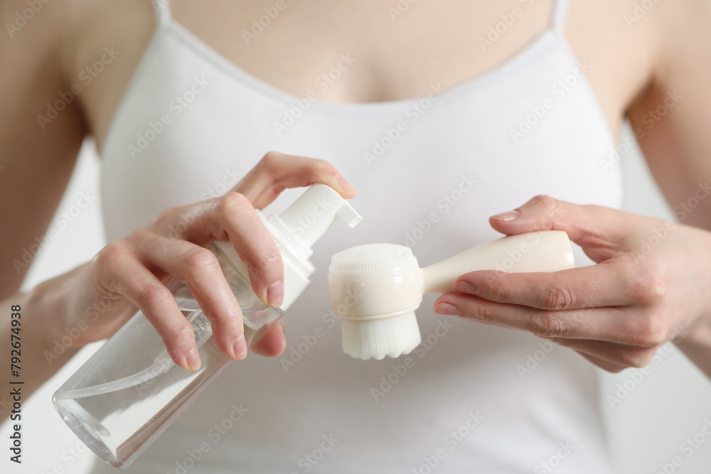 Wall mural Washing face. Woman applying cleansing foam onto brush against light background, closeup