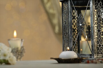 Arabic lantern and burning candles on table against blurred lights
