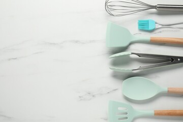 Different spatulas and other kitchen utensils on light marble table, flat lay. Space for text