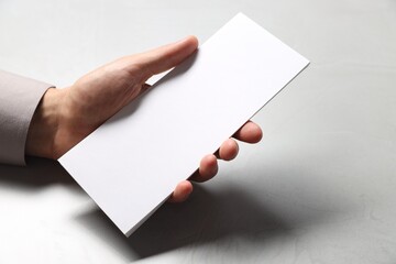 Man holding white blank card at light grey table, closeup. Mockup for design