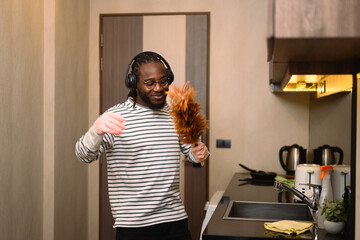 Happy young man doing chores listening to music with headphones and dancing - 792676905