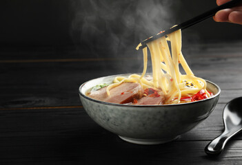 Woman eating hot ramen with chopsticks at black wooden table, closeup and space for text. Noodle...