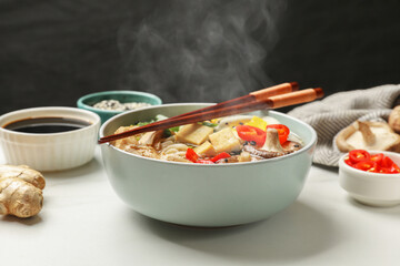 Bowl of hot ramen, ingredients and chopsticks on white table, closeup. Noodle soup