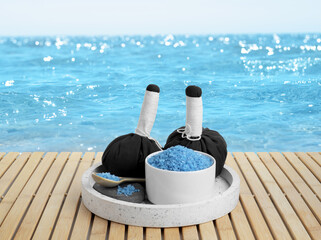 Bowl with blue salt and herbal bags on wooden table near sea