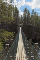 Wooden suspension bridge over river in cloudy spring weather at Kitkakoski rapids, Oulanka National Park, Kuusamo, Finland.