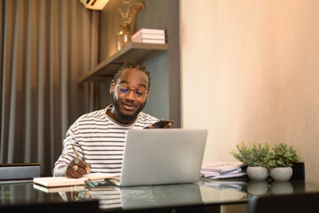 Smiling male entrepreneur working with laptop and making note at desk in living room - 792680952