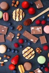 Macarons, chocolate, cookies, berries and various nuts on dark blue background. Top view.