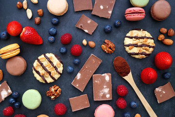 Macarons, chocolate, cookies, berries and various nuts on dark blue background. Top view.