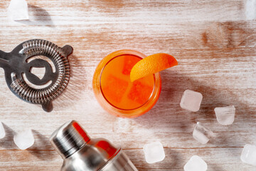 Orange cocktail and a shaker, with ice, overhead flat lay shot on a wooden background with copy space