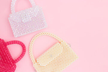 Various handmade bags made from acrylic beads scattered on a pink background with place for text.