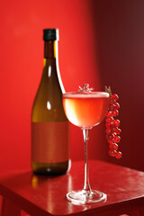glass with red alcoholic cocktail with red currants. A bottle of cordial in the background. Red background. nightlife, party, bar, restaurant.