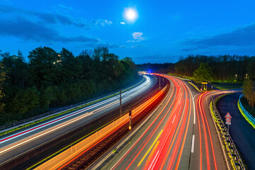 Evening panorama of “B54” expressway in the south of Dortmund in the Ruhr area (Germany). Curve with four lanes and a double-track tram route in blue hour. Colorful light trails from train and cars