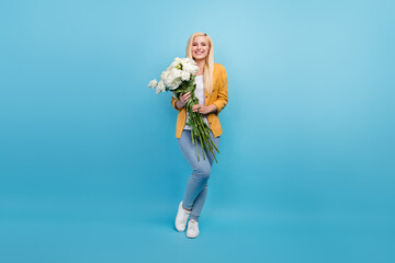 Full length photo of millennial blond funky lady hold flowers wear shirt jeans sneakers isolated on...