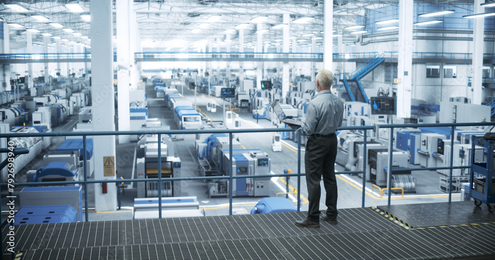 Poster Senior Factory Manager Working on Laptop at a Futuristic Industrial Manufacture with Autonomous AI Robots. Specialist Monitoring All the Data on a Computer, Checking Reports and Planning Workload