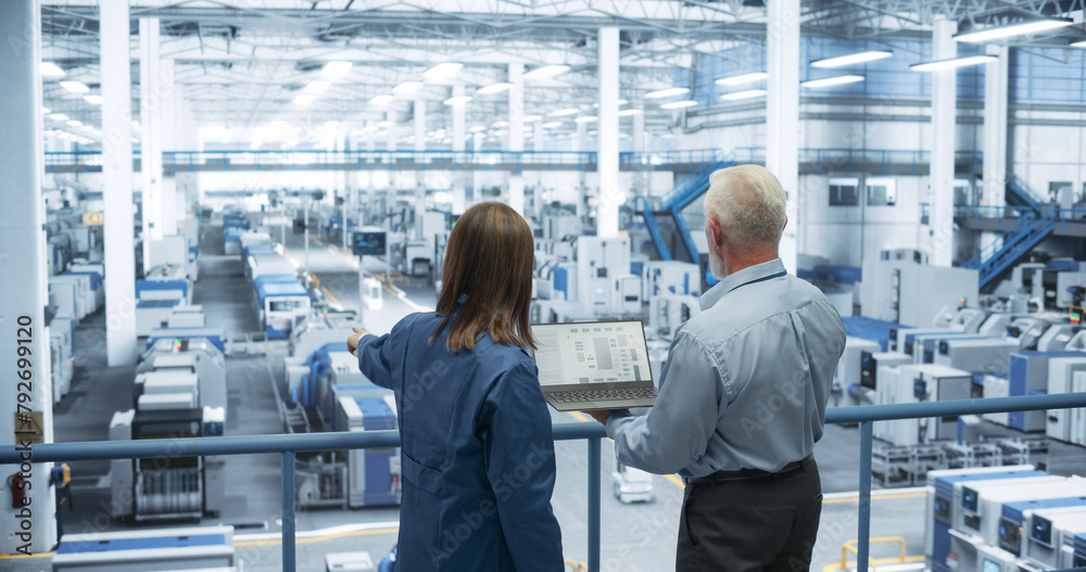 Aufkleber Experienced Male and Female Engineers Standing on a Platform, Using Laptop Computer and Discussing Production at a Modern Automated Electronics Manufacture with AI Support