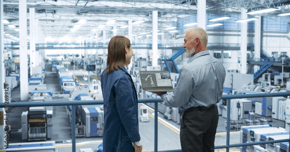 Fototapete Middle Aged Engineer and Young Japanese Technician Having a Conversation and Using Laptop Computer. Specialists Monitoring, Analyzing Conditions at a Modern Electronics Factory with Automated Robots