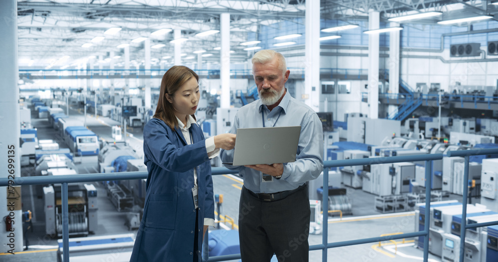Poster Male Engineer and Female Project Manager Standing on a Platform, Talking, Using Laptop Computer and Monitoring Production at a Modern Automated Electronics Manufacture with AI Robots